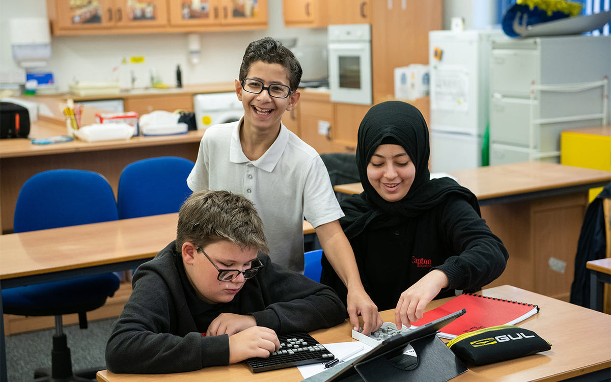 Three school pupils in a classroom using tactile maths tools.