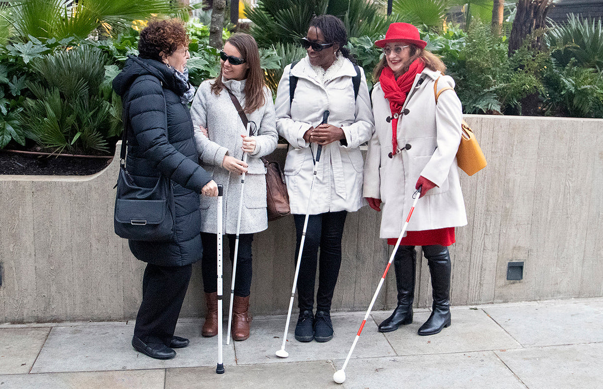 Four people standing on a street with various white canes and a white walking stick