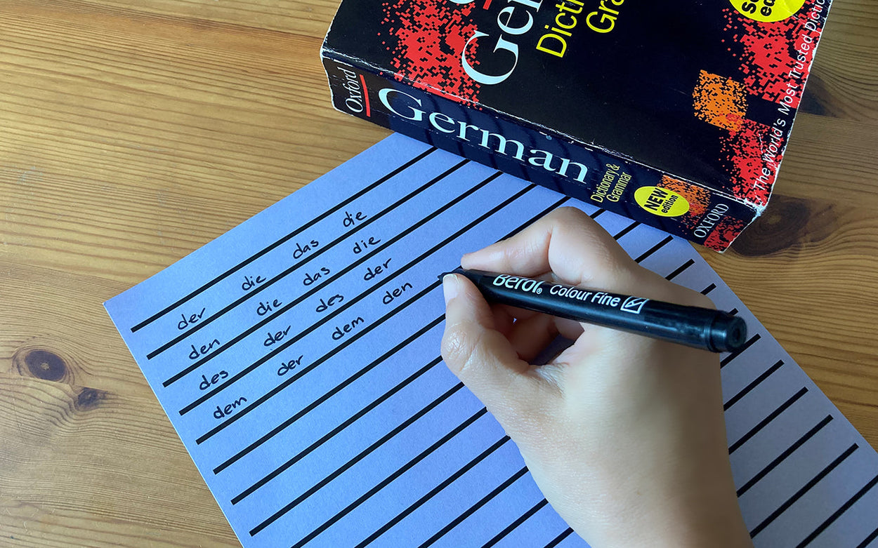 A person making notes on German grammar on lilac coloured, thick-lined paper