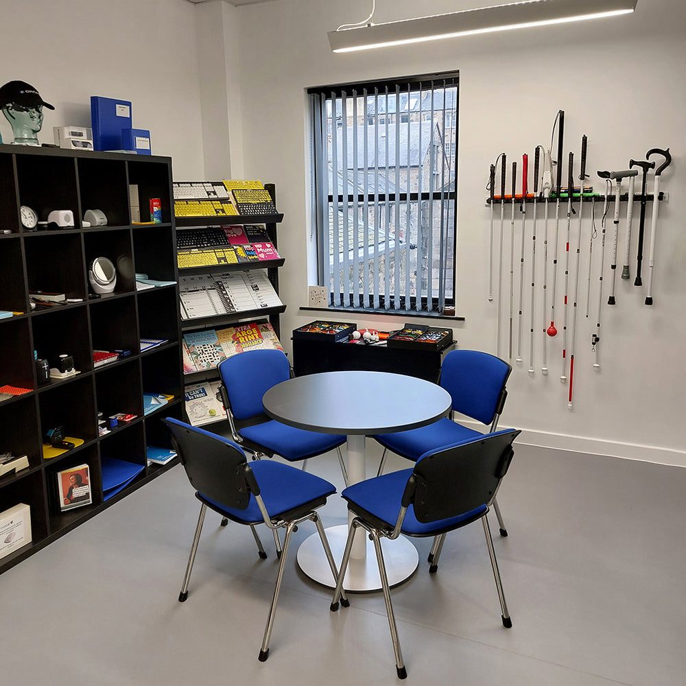 Edinburgh store. A small table with four chairs placed around it. On one wall is a rack showing canes and walking sticks, on another is shelving displaying a selection of accessible products.