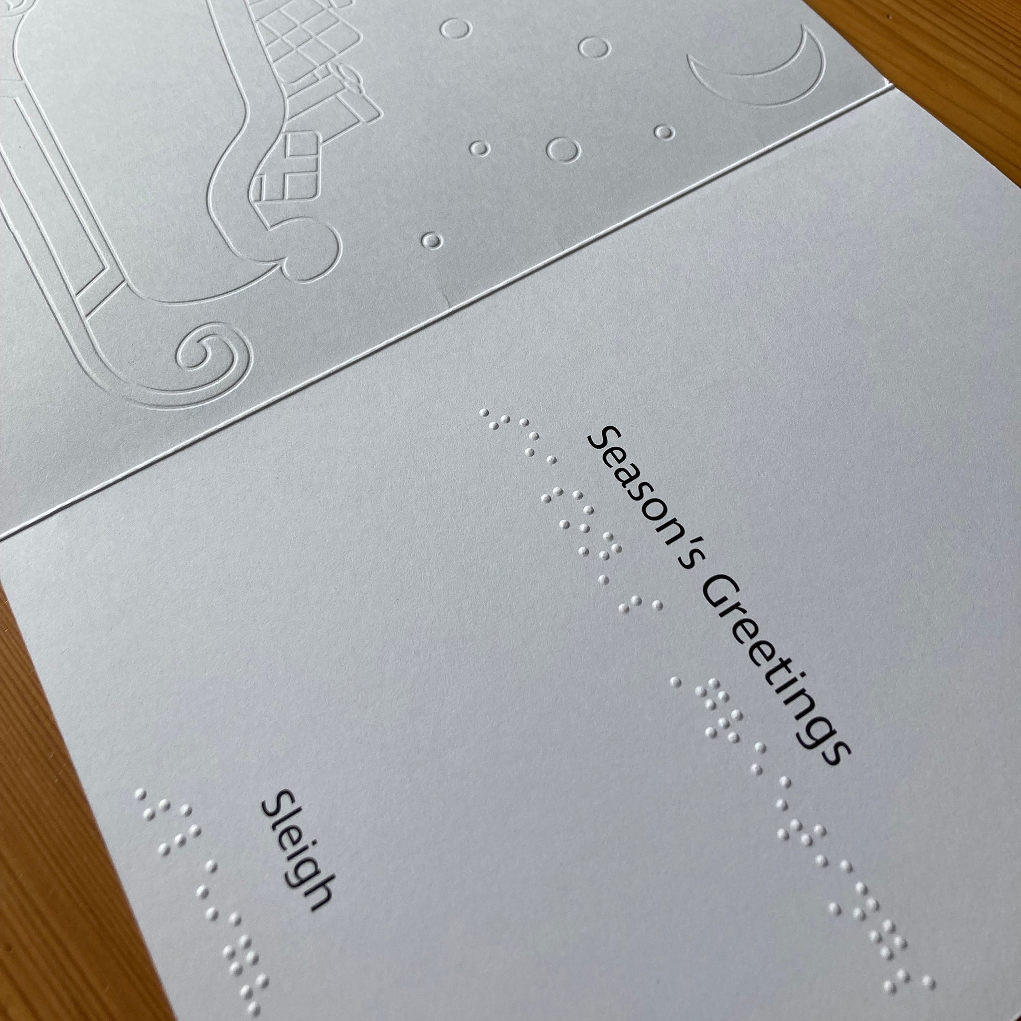 White card with 'Season's Greetings' and 'Sleigh' text and braille, embossed with a sleigh design.