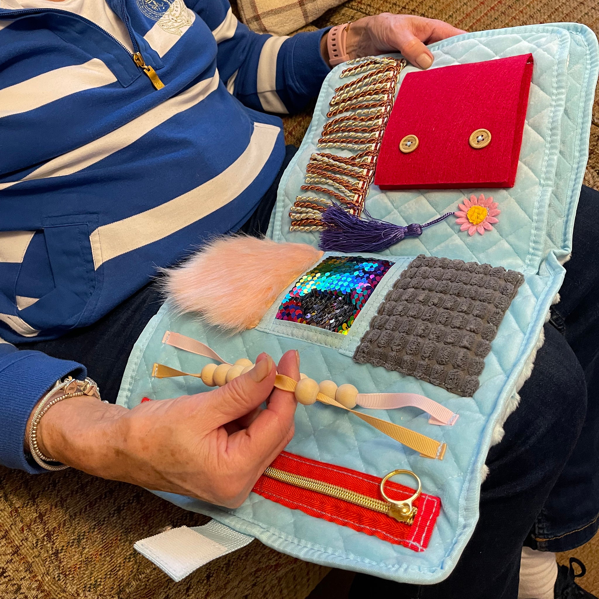 A person using the fiddle blanket on their lap whilst sitting on a sofa.