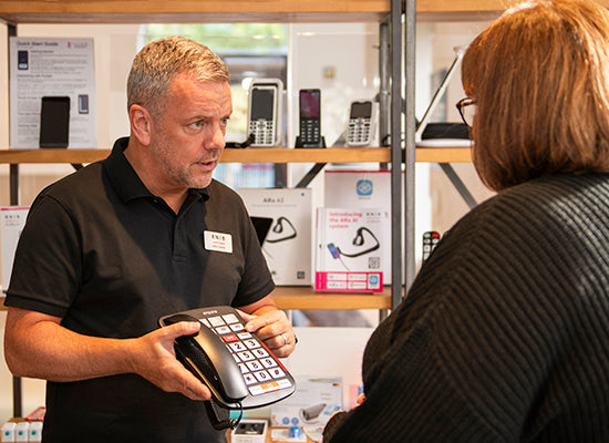 Products and advice centre staff demonstrating a big button phone to a customer