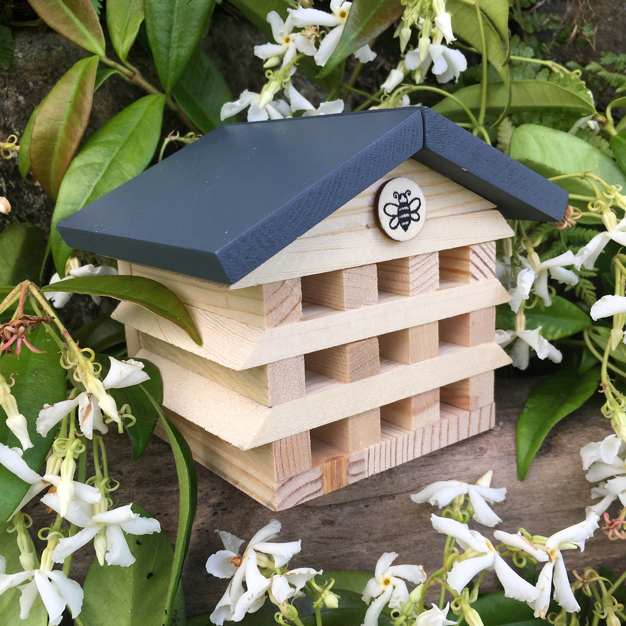 Wooden bee house with a blue roof on a natural background with flowers and leaves.