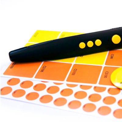 An RNIB PenFriend on top of two sheets of coloured labels in various shapes and sizes