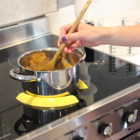 Yellow pan pickles holding a pot in place on an induction hob while food is stirred