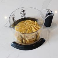Two black pan pickles holding a measuring jug containing dry pasta in place on a worktop