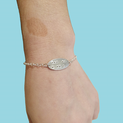 Adjustable silver bracelet with ‘mum in braille being worn