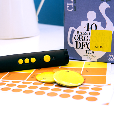 RNIB PenFriend 2 with sheets of recording labels next to a box of tea bags with a yellow label