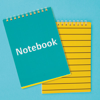 Two notebooks, one open showing yellow paper and one closed showing the cover which says Notebook