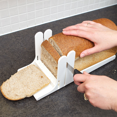 A person slicing bread using a white bread slicing guide with tactile markings