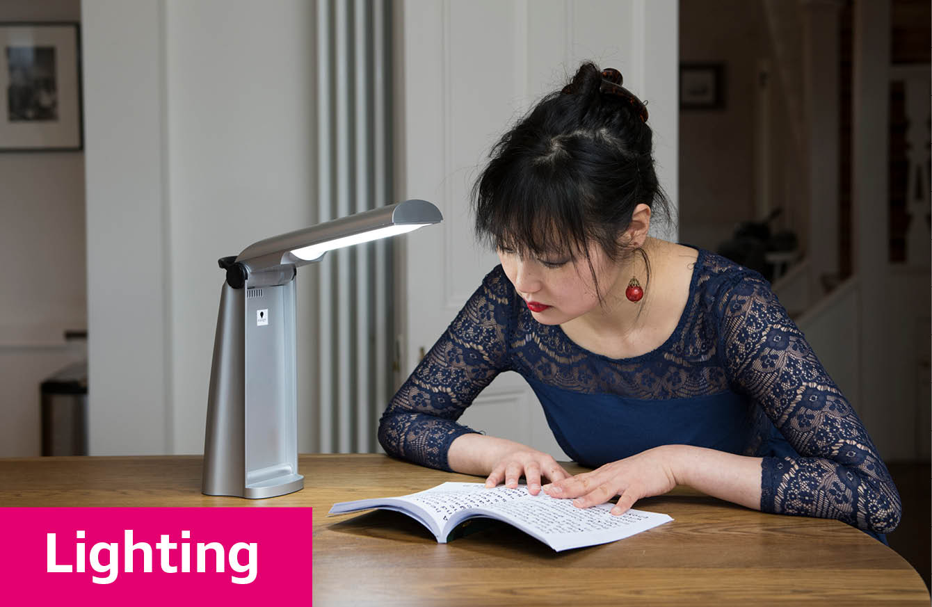 A young woman reading at a table using a desk light