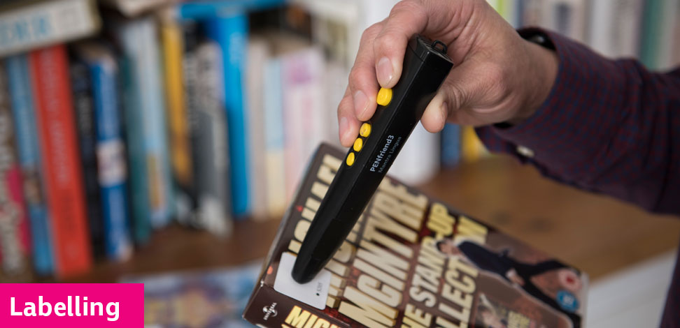 A person using a PenFriend to read a label on a DVD cover