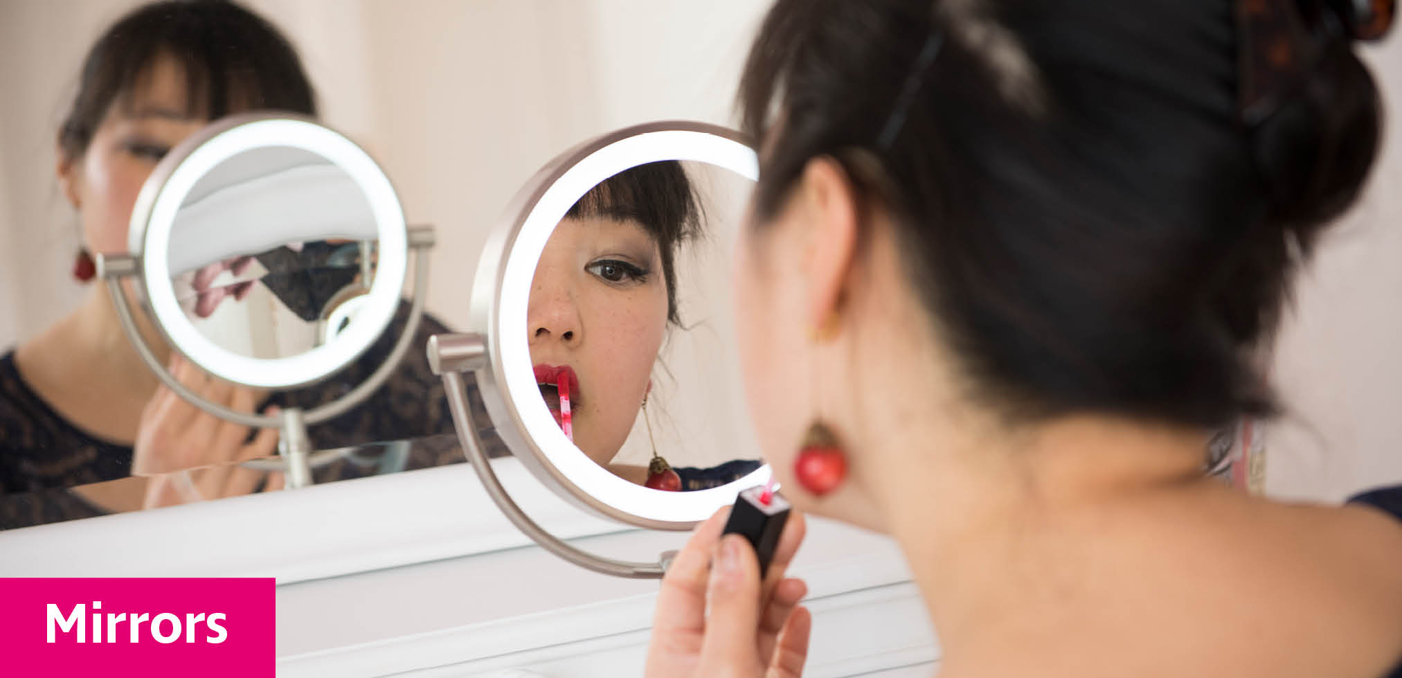 A young woman using a magnifying mirror to apply lipstick