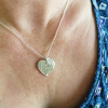 Heart-shaped silver necklace with ‘mum’ in braille and charm being worn