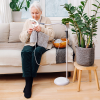 An older white woman knits on a sofa using the light and magnifier