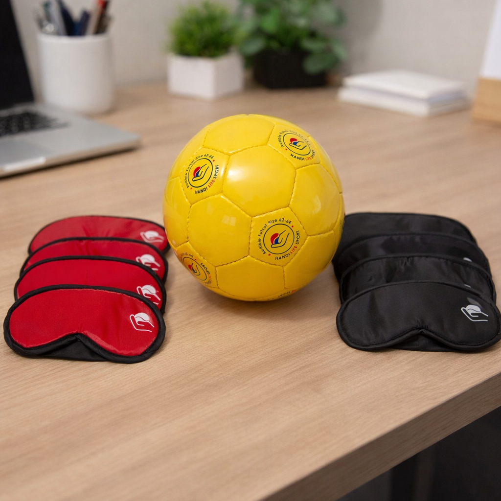 Blind football starter kit showing a yellow audible futsal ball with two sets of eye masks — four red and four black — laid out on a desk