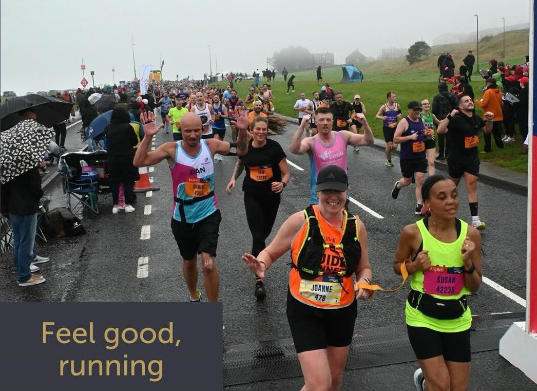 Susan and Jo cross the finish line at the Great North Run. Behind them are more runners, and supporters lining the route.