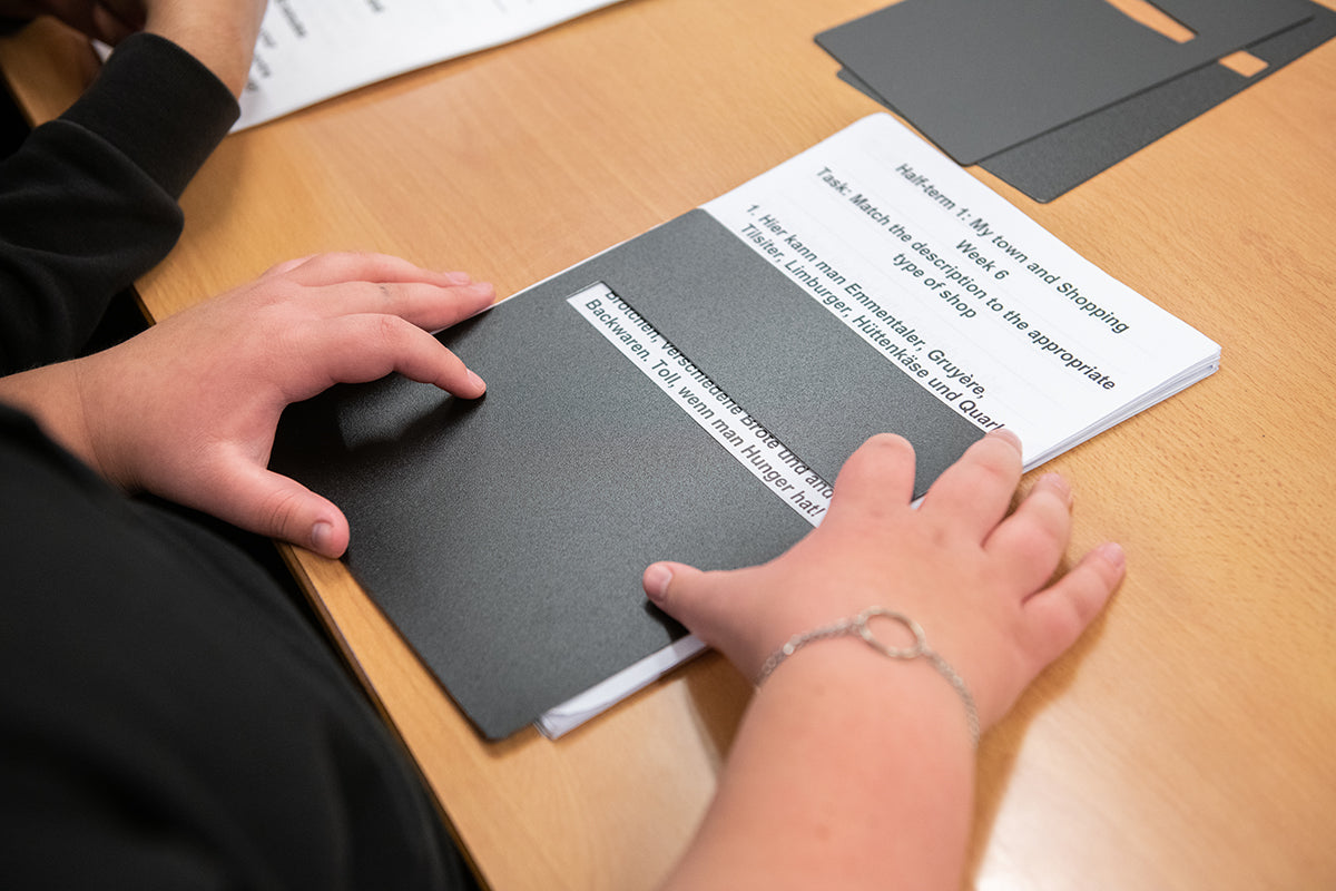 A young person using a reading guide (or typoscope) to read large print learning materials in a classroom