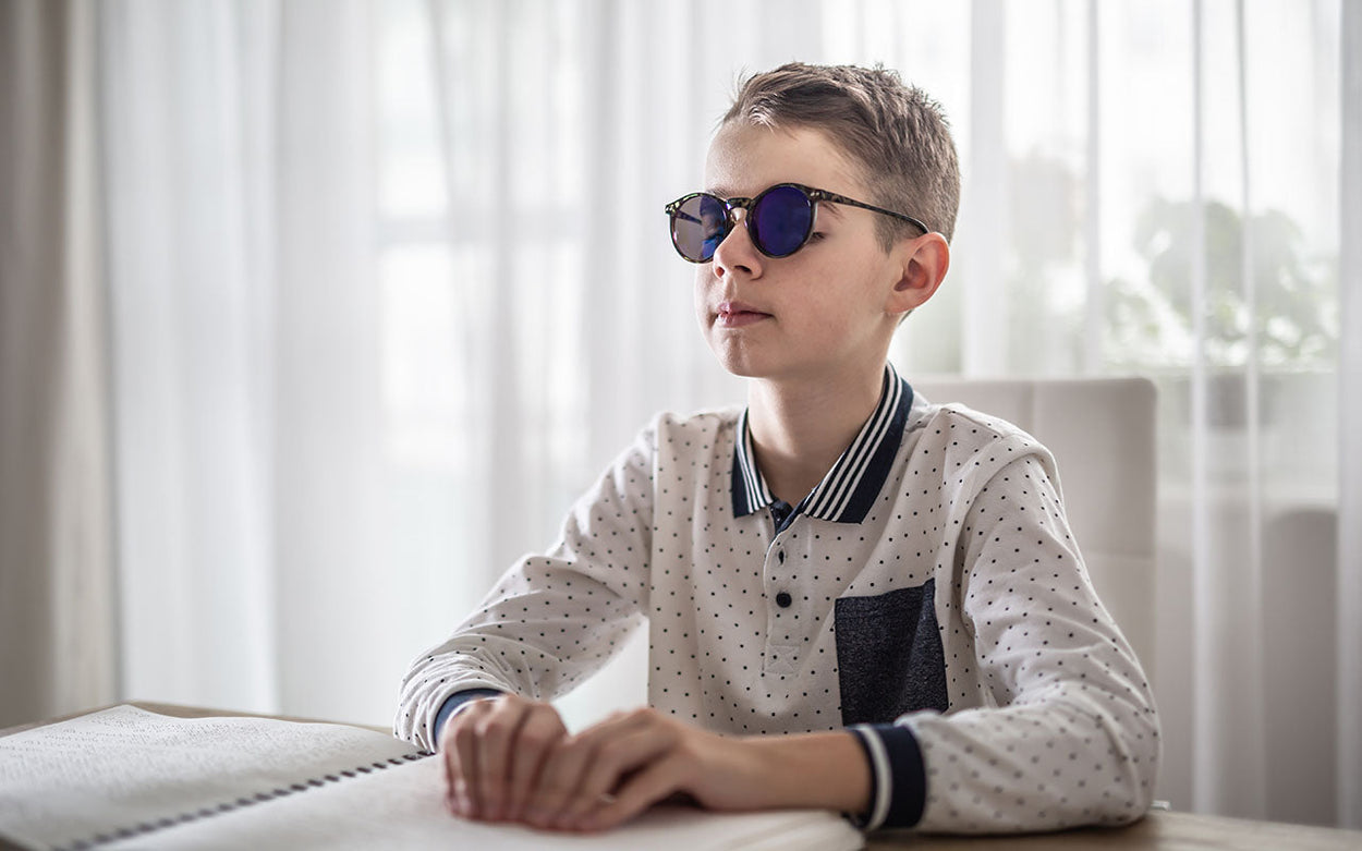 A boy sitting at a table and reading a braille book.