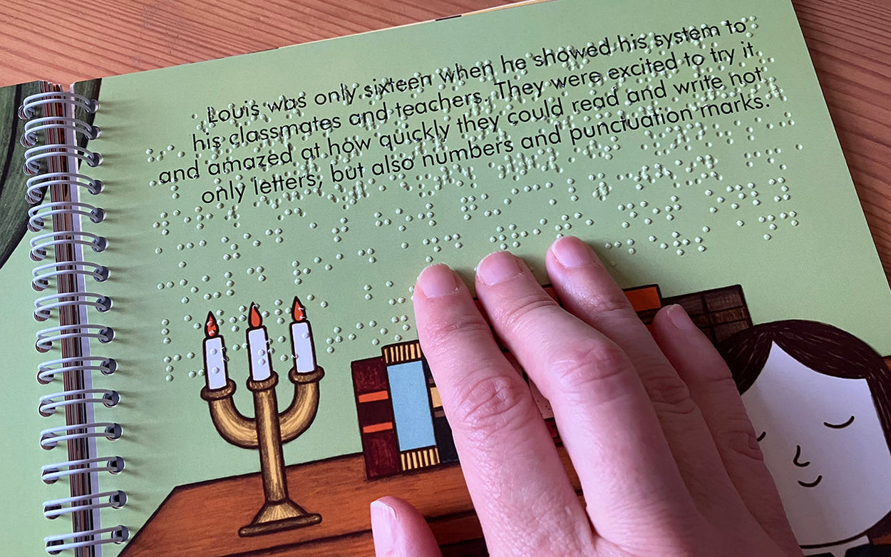 Fingers reading braille in the print and braille edition of Little People, Big Dreams: Louis Braille.
