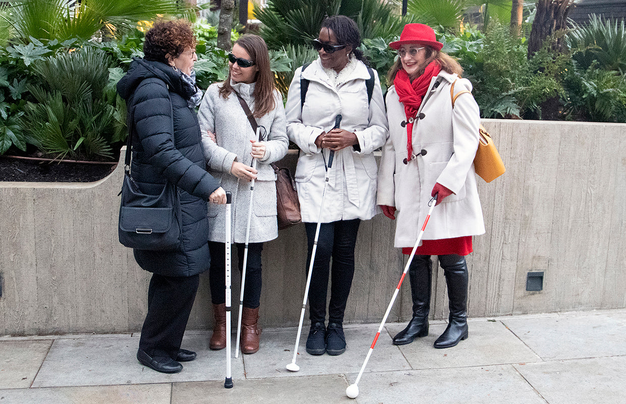 Four people standing on a street with various white canes and a white walking stick