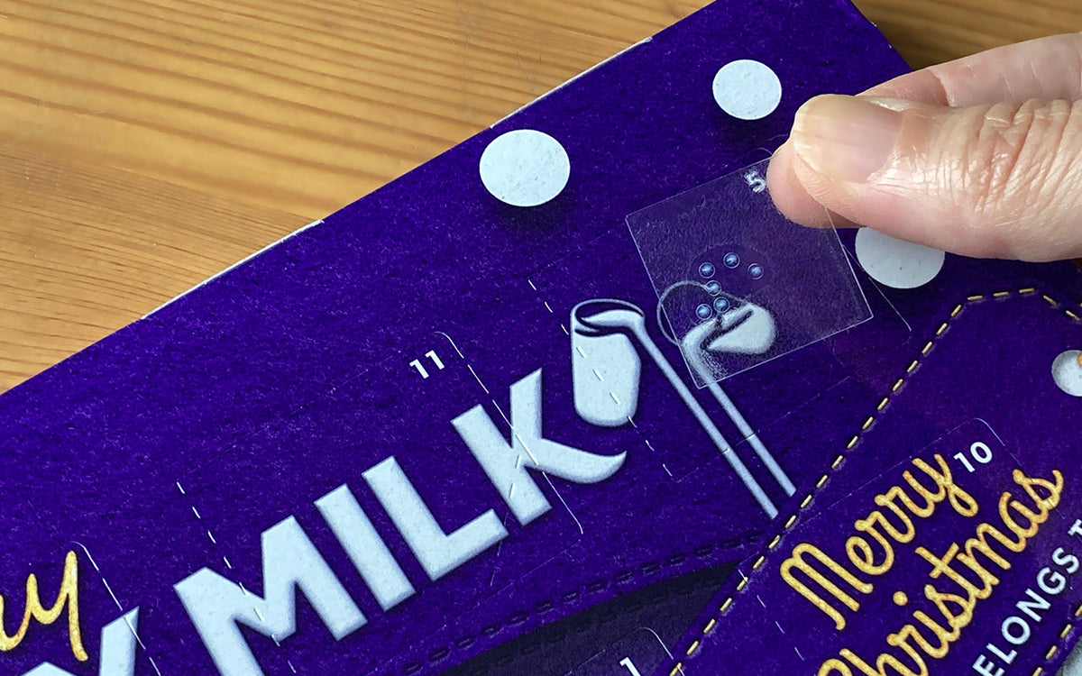 A person applying a clear braille sticker to door no 5 on a chocolate Advent calendar