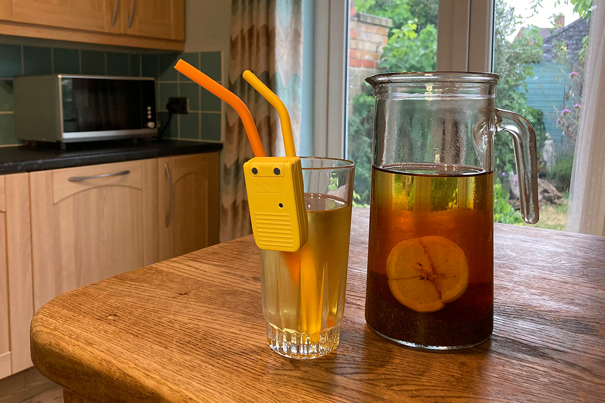 Liquid level indicator on a drinking glass that contains iced tea and two straws. The glass is on a wooden breakfast bar next to a glass jug of homemade iced tea