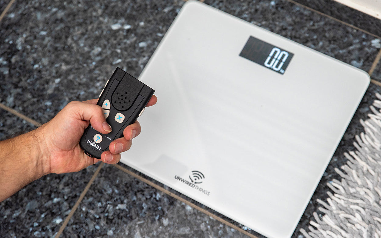 A hand holds an IKONN controller above the IKONN digital bathroom scales.