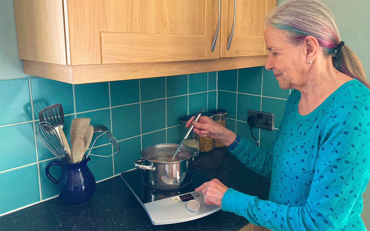 An older white woman in a turquoise top using the RNIB talking induction hob on a kitchen counter.