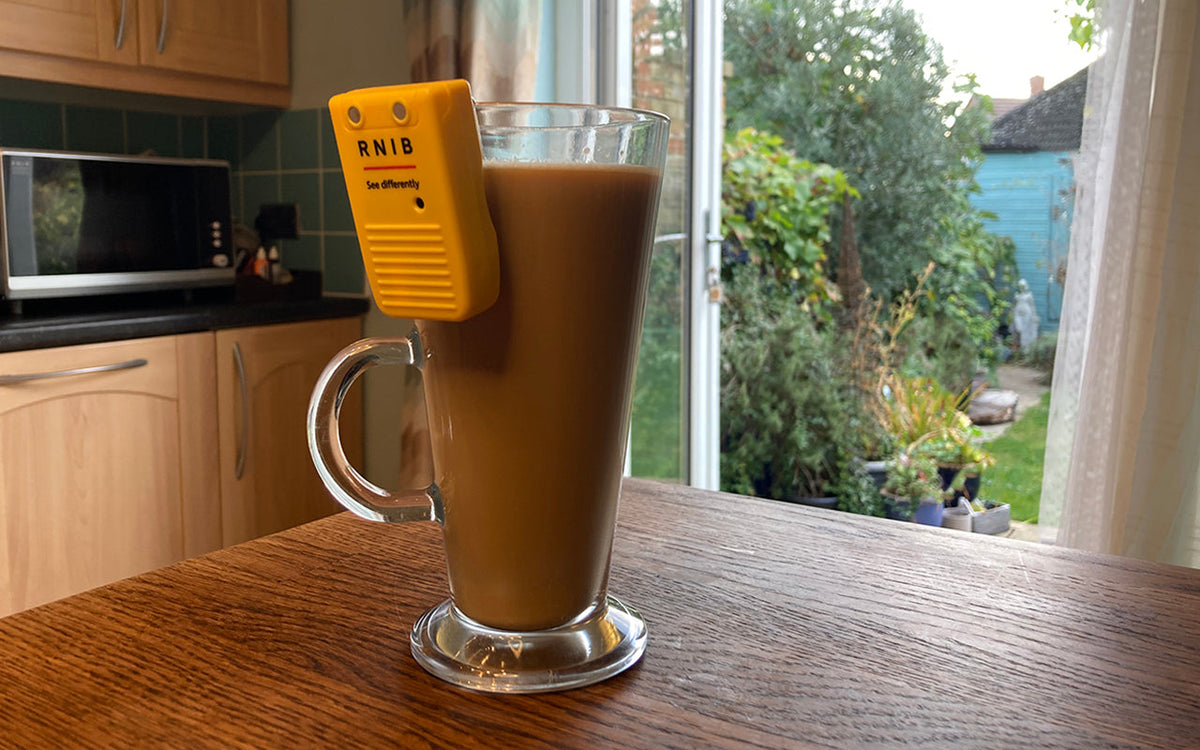 A tall glass cup filled with coffee and with a liquid level indicator on the rim on a wooden surface in a kitchen