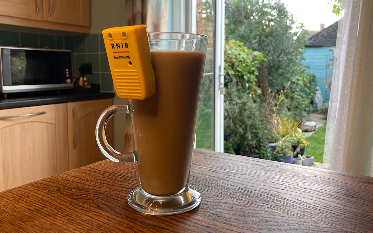 A tall glass cup filled with coffee and with a liquid level indicator on the rim on a wooden surface in a kitchen