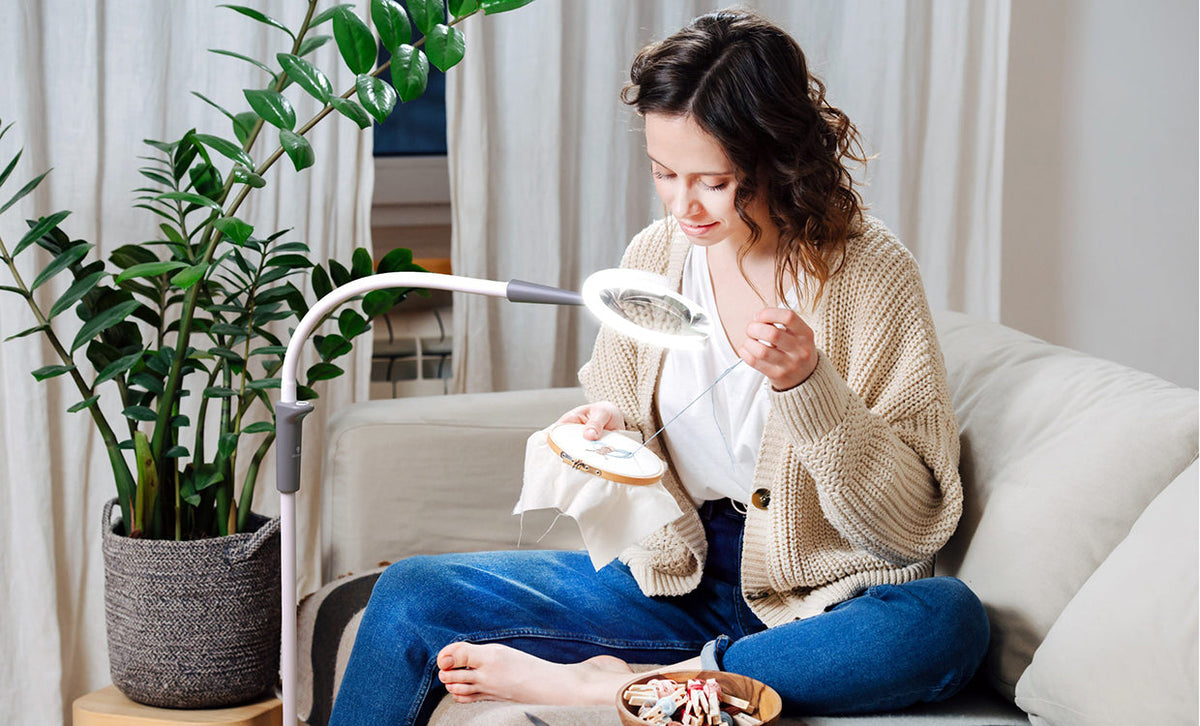 A white woman using a magnifier lamp to help with her embroidery.