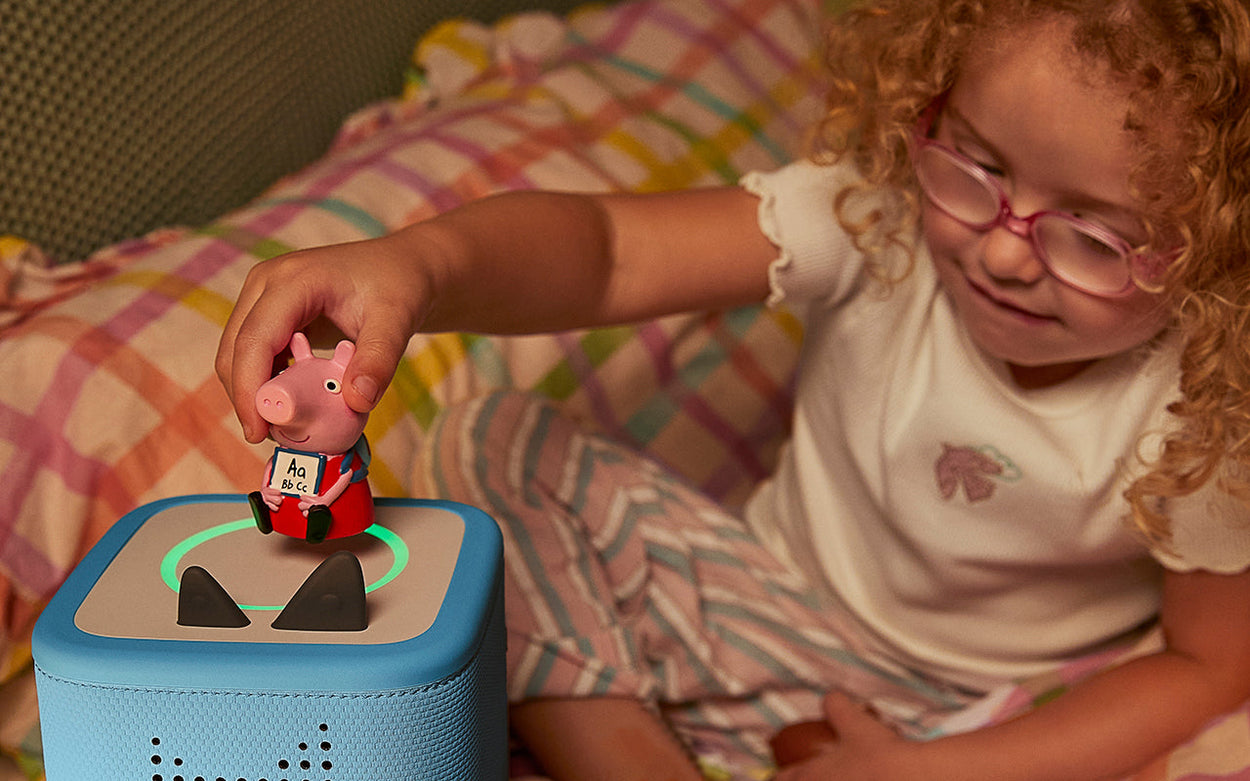 Young child wearing pink-framed glasses placing a Peppa Pig Tonie on a blue Toniebox