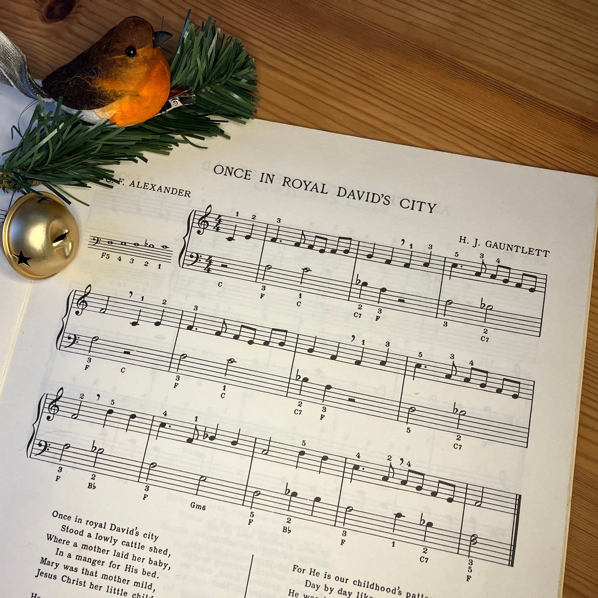 Piano sheet music for Once in Royal David's City with a golden bell, sprig of fake Christmas greenery and a robin decoration
