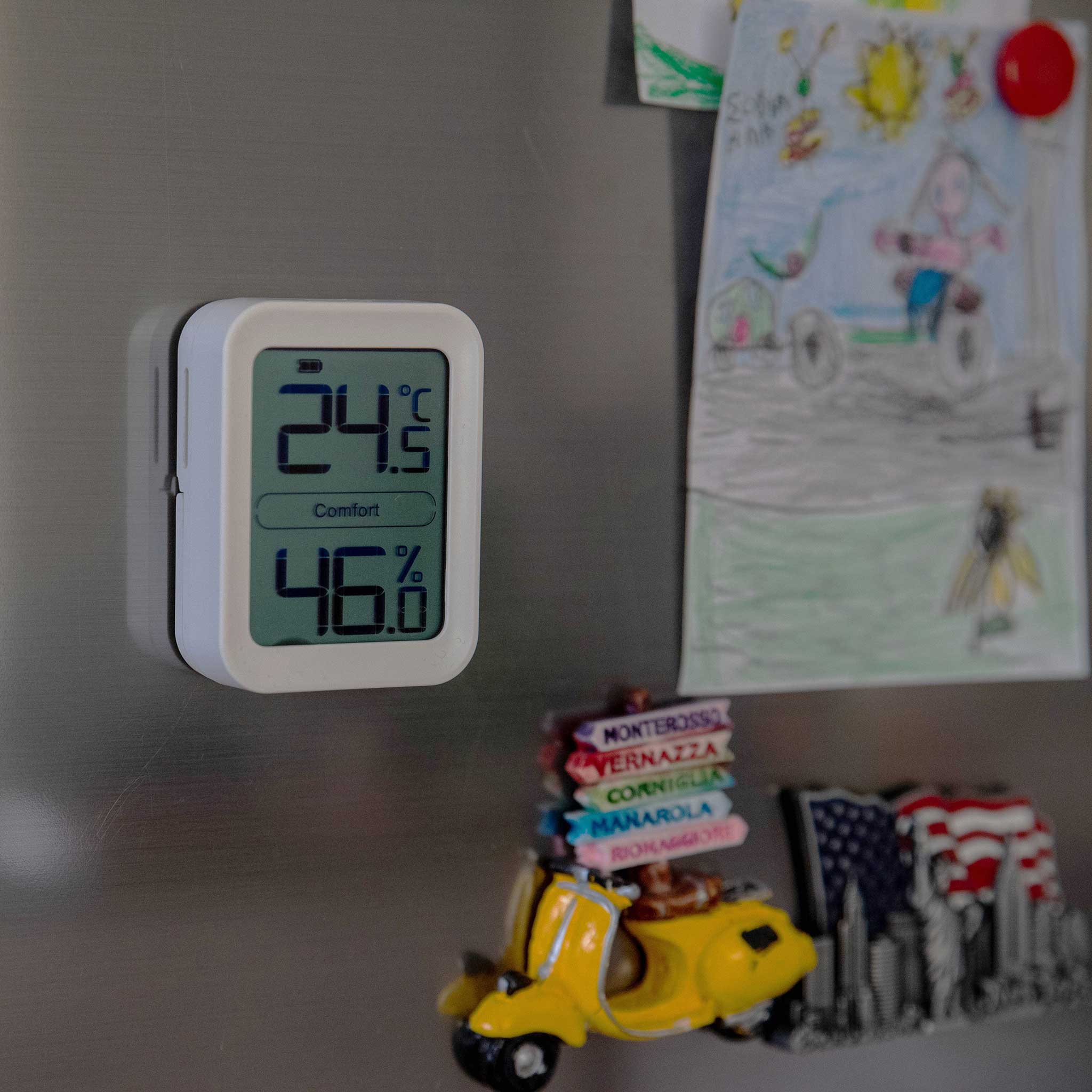 Ikonn indoor thermometer on a refrigerator with children's drawings and magnets.