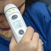 Digital thermometer being used to measure temperature with a person wearing a blue shirt in the background.
