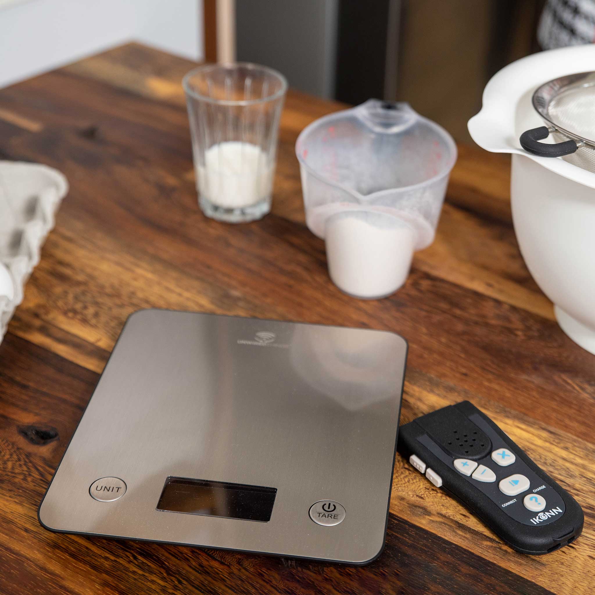 Digital kitchen scale on a wooden table with measuring cups and Ikonn control in the background.