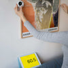 Person using the tape measure o measure the width of a poster on a white wall.