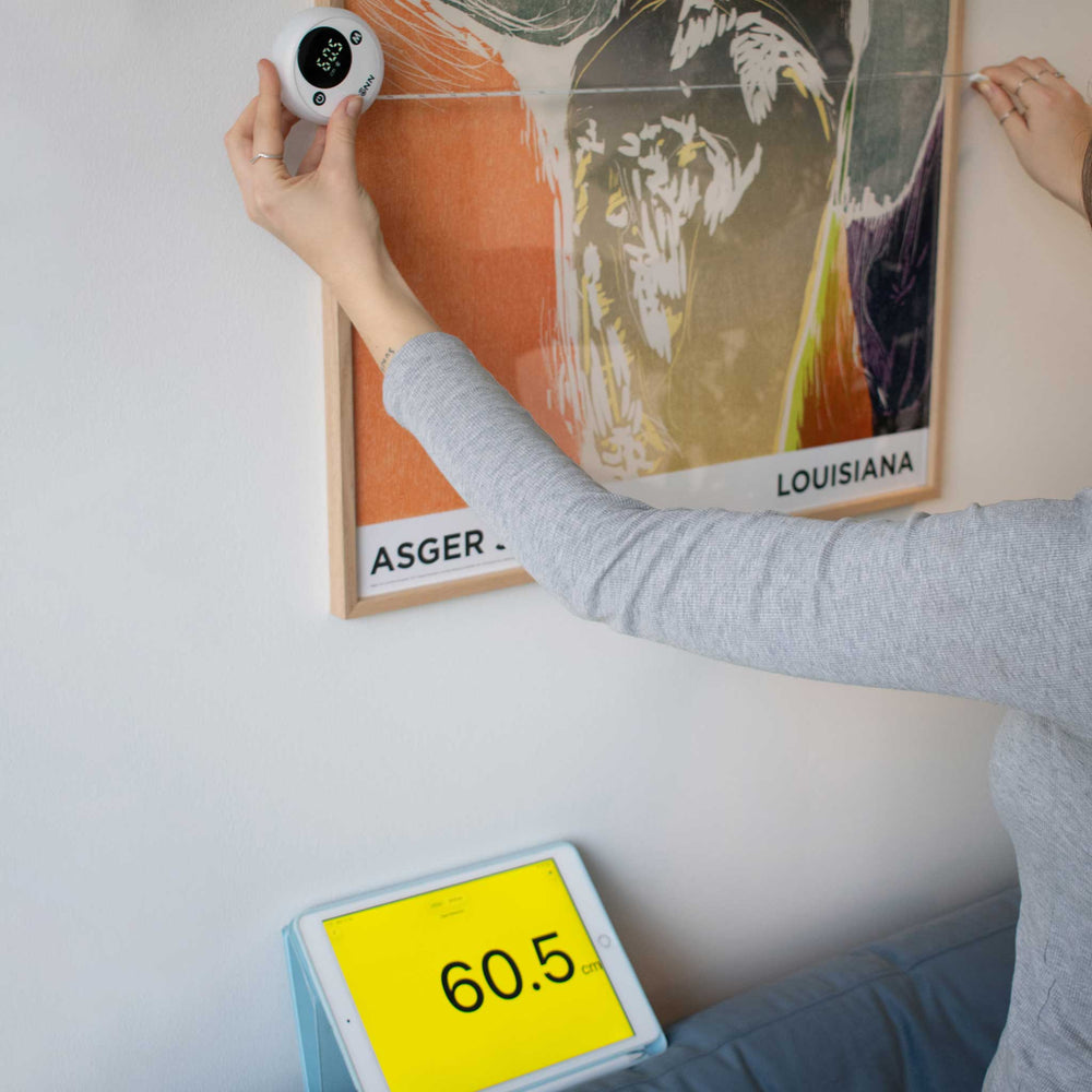 Person using the tape measure o measure the width of a poster on a white wall.