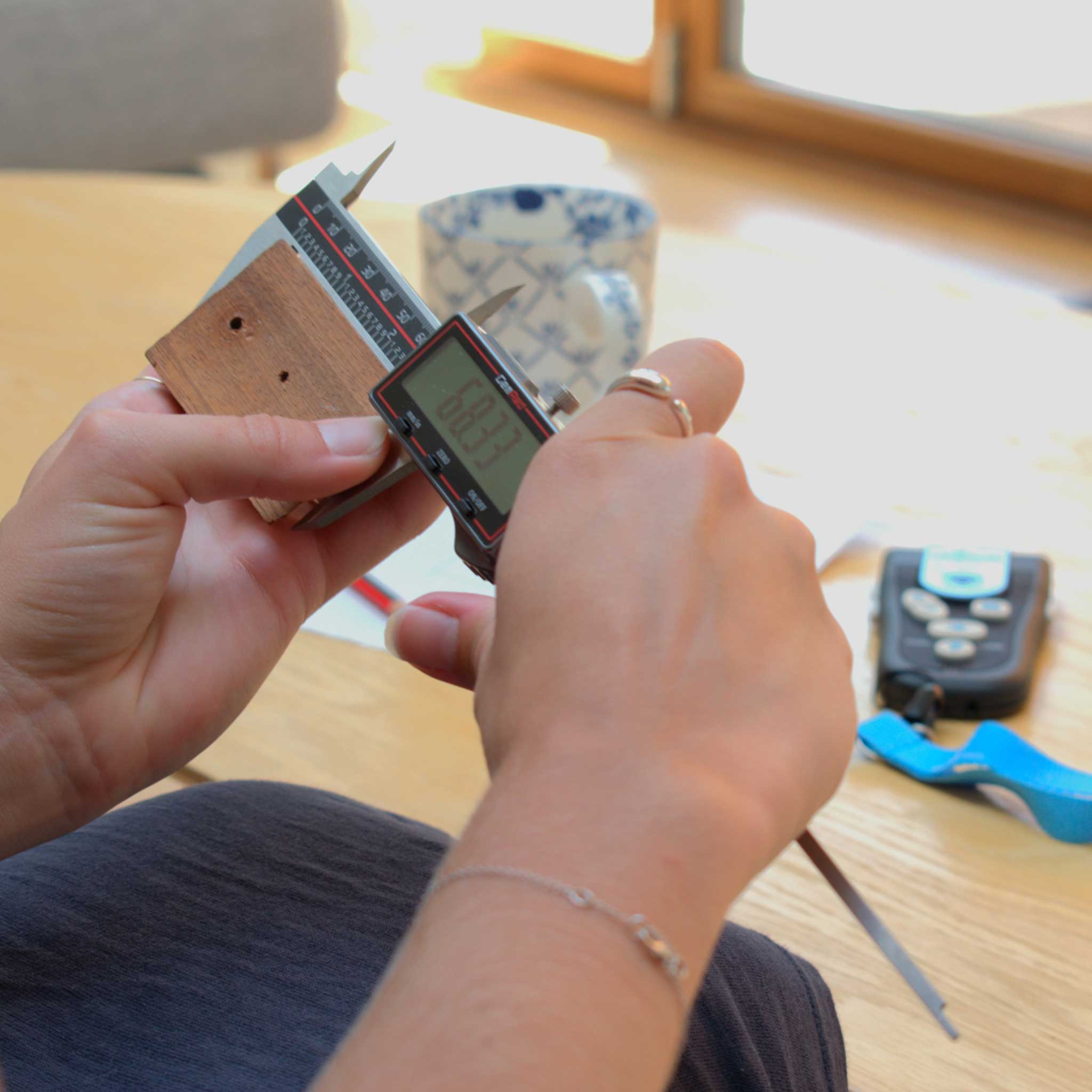 Person using a digital tool on a wooden surface with tools and a cup in the background