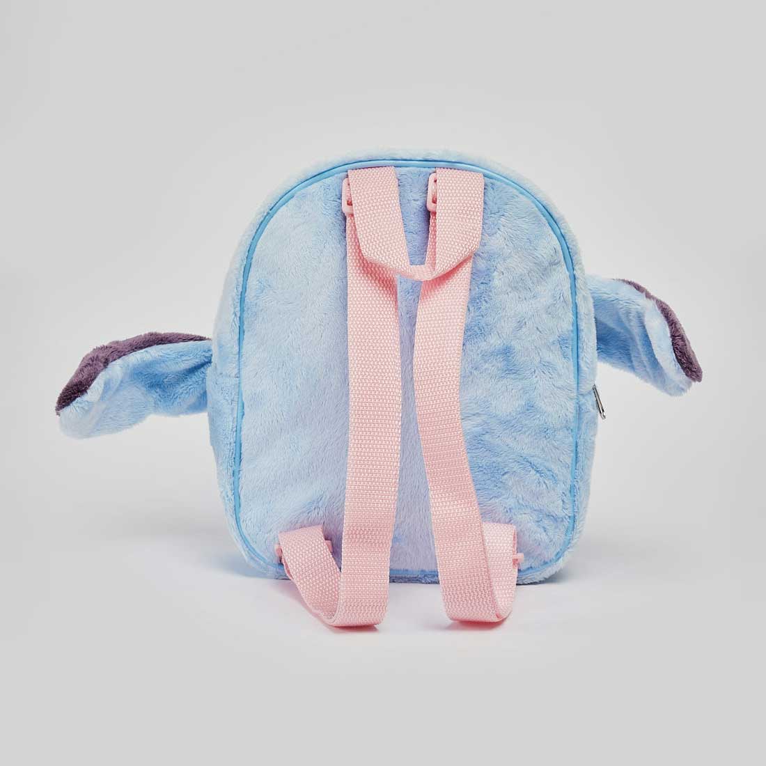 A plush character backpack shaped like Stitch, shown from the back. The backpack is light blue with pink straps and darker purple inner ears, set against a plain light gray background.