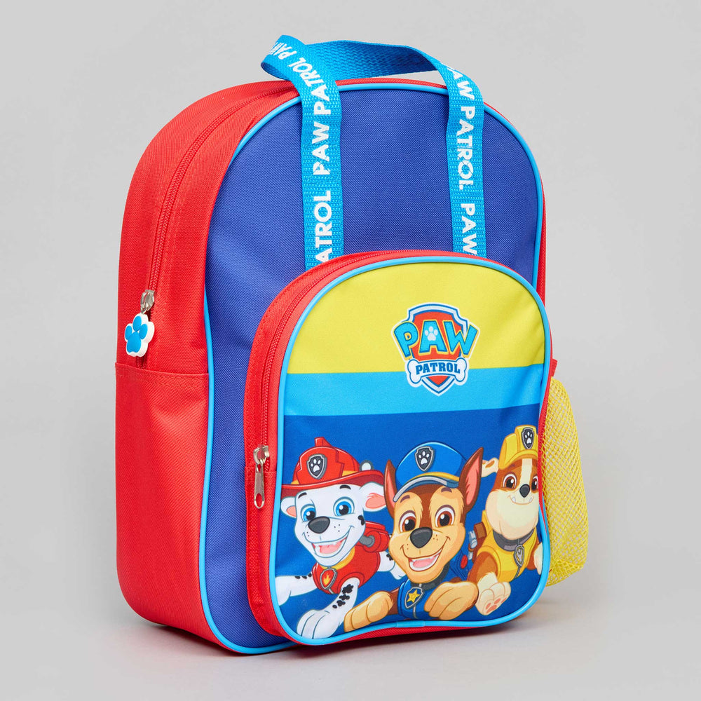 A Paw Patrol themed children's backpack featuring a red body, blue top panel, yellow front accent, and character graphics on the front pocket. The straps are blue with white Paw Patrol text, and the backpack is photographed on a neutral light gray background.
