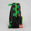 A black backpack featuring a green and orange Minecraft-themed pattern, including pixelated block graphics, a green TNT keychain, and bright green zippers and straps, shown against a neutral gray background.