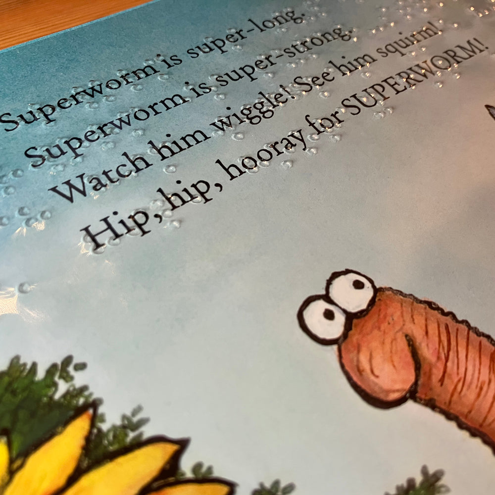 Children's book page with a cartoon worm with text and braille about Superworm.