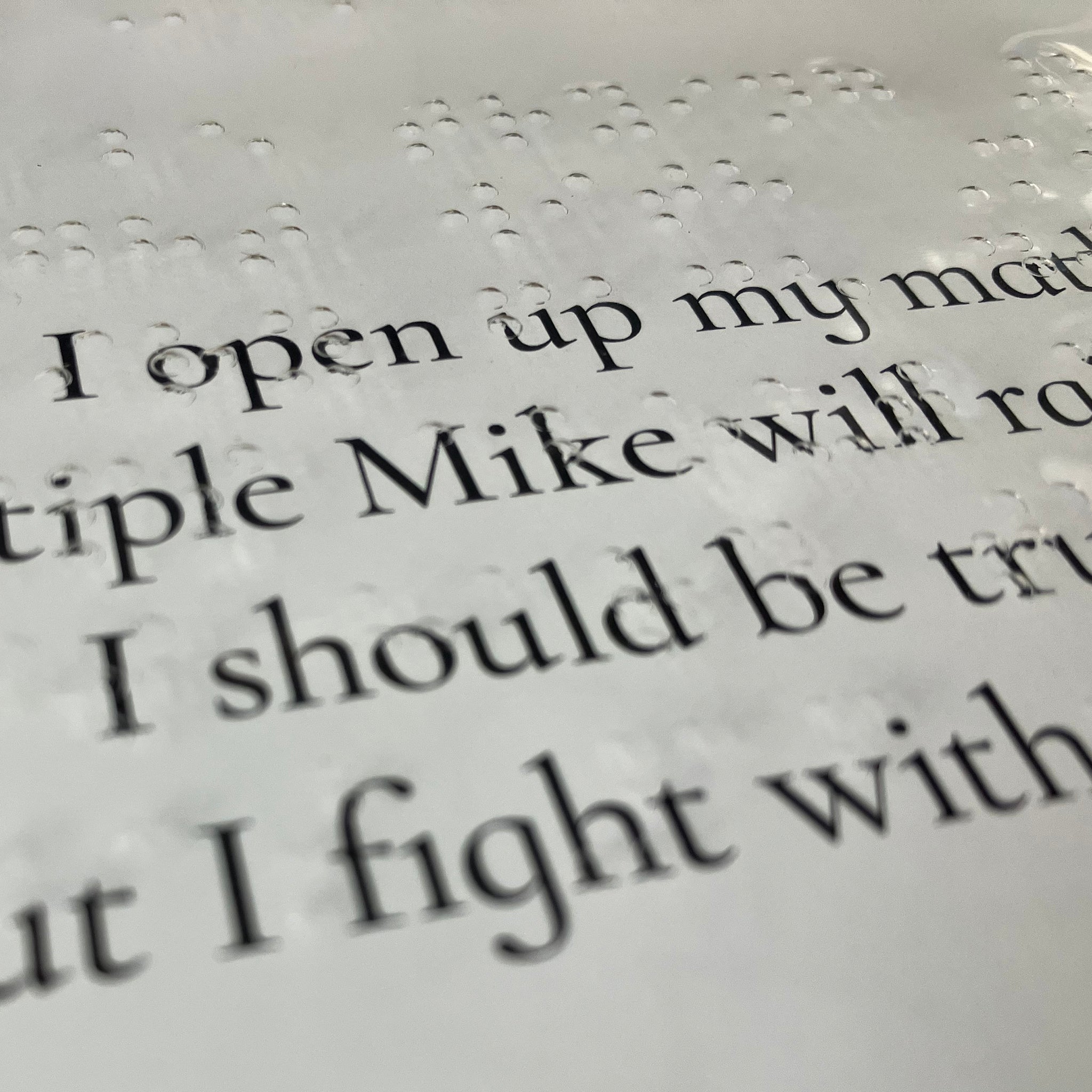 Close-up of clear braille sheet over original text in the book.