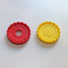 A red and yellow Connect 4 counter side by side. The red counter has a hole in the middle, the yellow counter does not.