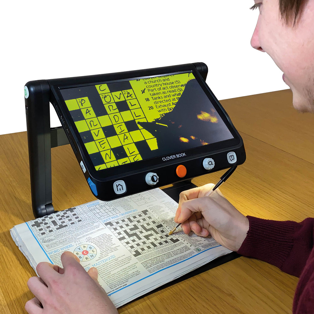 CloverBook Lite being used to scan a newspaper crossword. The image of the crossword onscreen is in black and yellow and the person is using a pen to complete the crossword on the newspaper.