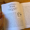 Open book with a page titled 'The Mask' held by a hand on a wooden surface
