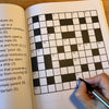 Crossword puzzle in a book with a hand holding a pen, partially filled in